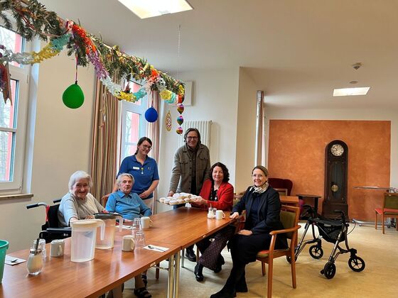 Sibylle Entwistle, Ruth Müller, MdL, und Johann Luger übergeben die Krapfen Ashley Cassada (in blau) und di